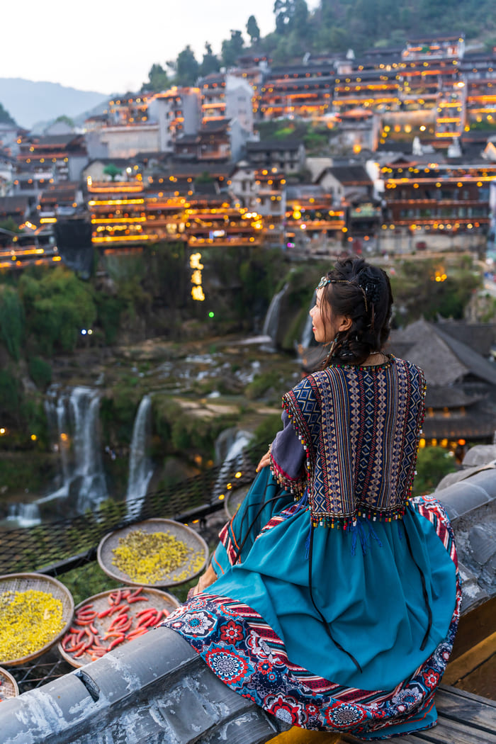 Mujer china, admirando sentada y dessde lejos la ciudad Lijiang